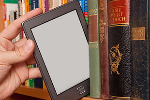 person holding black monitor near pile of books